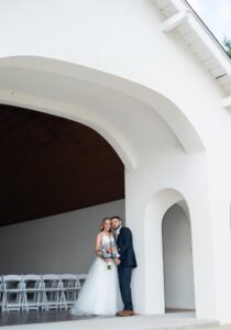 Bride and groom share a tender moment under a white arch.