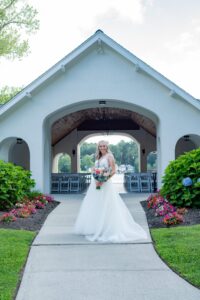 Bride in white gown standing under a charming archway with floral decorations.