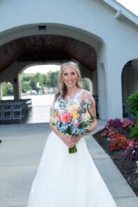 Bride in white dress holding a colorful bouquet outdoors.