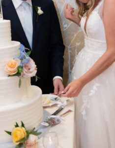 Bride and groom cutting a white wedding cake adorned with flowers.