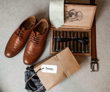 Men's brown leather shoes with accessories including a watch, belt, and cigar set.