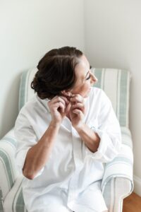 Woman putting on earrings while sitting in a chair.