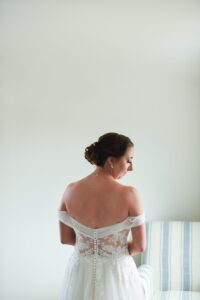 Bride with elegant updo and lace off-shoulder dress looking sideways.