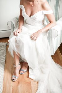 Bride sitting on a white couch, adjusting her shoe strap.