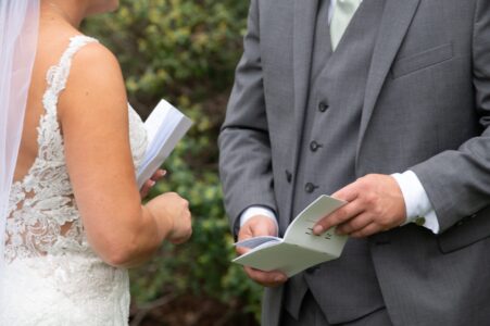 A couple exchanging wedding vows outdoors, holding papers.