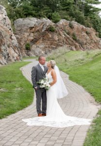 A bride and groom share a kiss on a winding stone path by rocky hills.