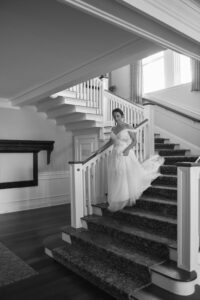 Bride in a flowing gown descends elegant staircase in classic black and white.