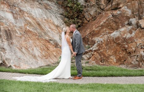 Bride and groom share a moment outdoors by a rocky backdrop.