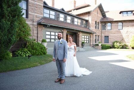 Bride and groom standing in front of a large house on their wedding day.