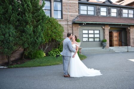 Bride and groom share a kiss outdoors in front of a house.