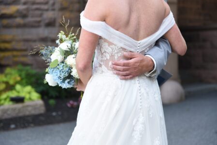 Bride and groom embracing, showcasing wedding dress details and bouquet.