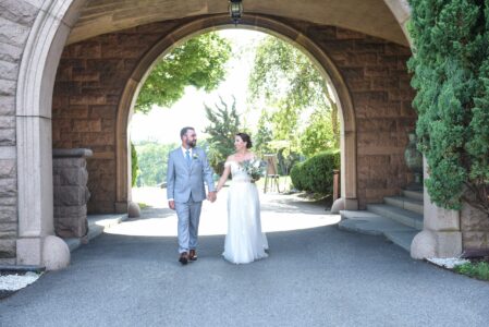 Newlywed couple walking hand in hand under an archway on their wedding day.