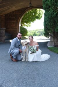 Newlyweds posing with their dog outside a rustic venue.