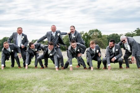 Men in tuxedos forming a human pyramid outdoors on grass.