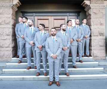 Groom and groomsmen in matching gray suits pose on church steps.