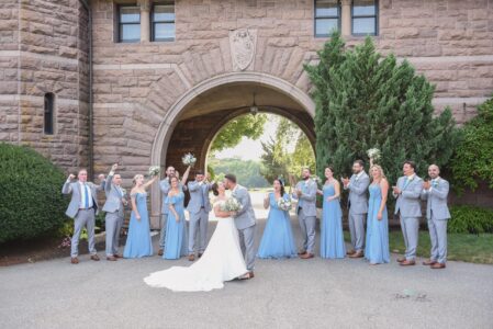 Bride and groom kiss surrounded by bridesmaids in blue dresses outdoors.