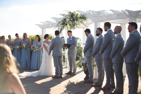 Couple exchanging vows at an outdoor wedding with bridal party beside them.