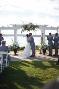 Bride and groom share a kiss under a floral arch during an outdoor wedding ceremony.