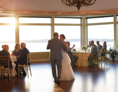 A couple dancing at their wedding with guests watching in a sunlit room.