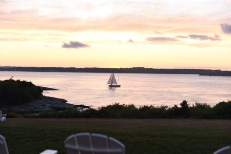 Sailboat glides on calm water during sunset with soft clouds overhead.