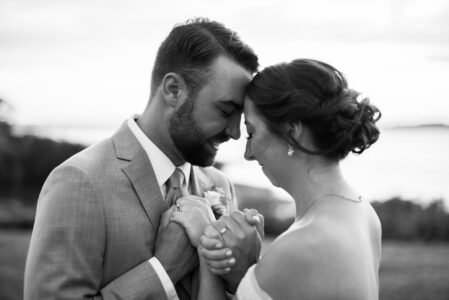 A couple shares a tender moment, holding hands and touching foreheads.