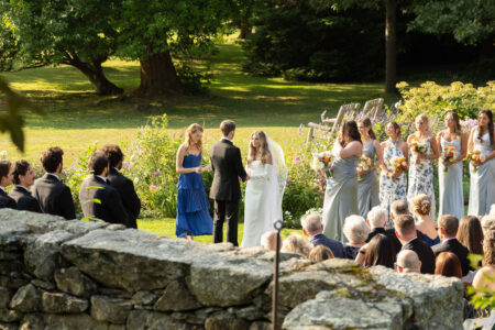 Outdoor wedding ceremony with bride, groom, and guests in a lush garden.