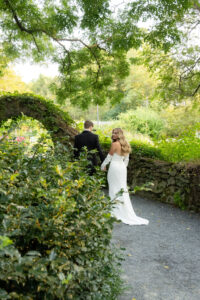Bride and groom walking along a garden path surrounded by greenery.